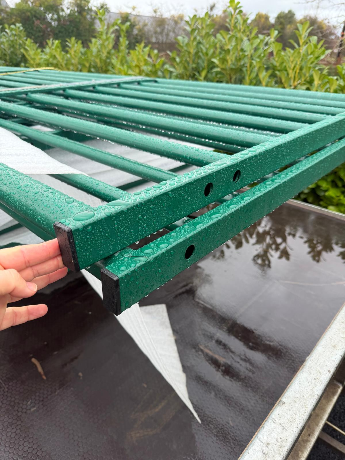Green powder coated metal gates stacked outdoors with water droplets